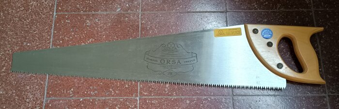 Gammal fogsvans från JärnBirger i Orsa, cirka sextio år gammal, med träskaft och blad liggande på ett mörkt golv.