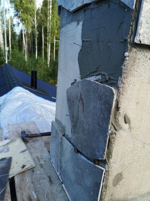 Murad skorsten med stenplattor fästa med tråd och murbruk, skog i bakgrunden.