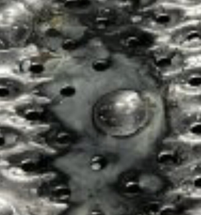 Metallyta med hål och mörka fläckar som liknar smuts eller avlagringar.