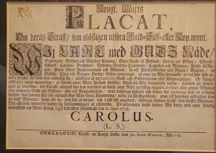 Ett gammalt plakat från Karl XII:s tid, med text om straff för olovligt utförande av mynt. Hål i övre vänstra hörnet från syre-bläck numrering.