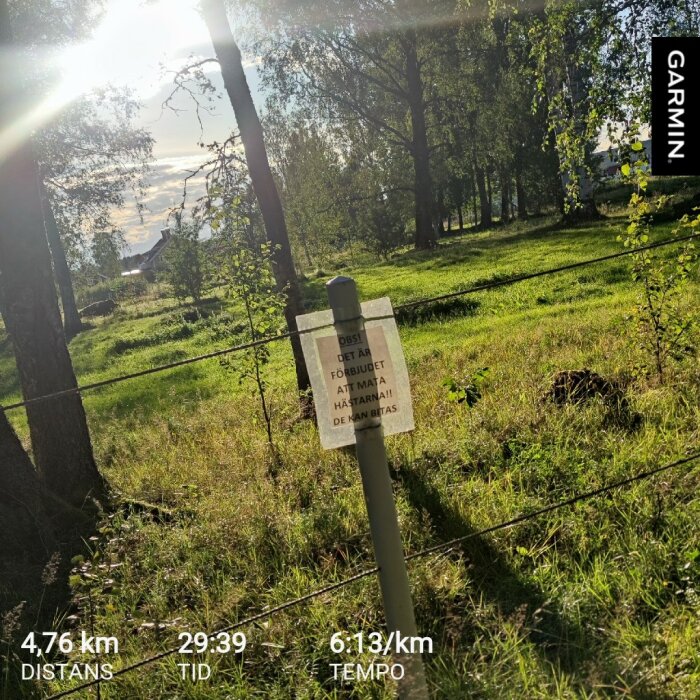 Skylt vid en hage i soligt landskap, varnar för att mata hästar eftersom de kan bitas. Garmin-data för distans, tid och tempo visas längst ner.