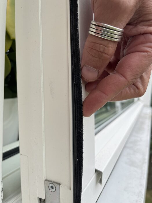 Närbild på en hand som drar ut en svart list från en vit fönsterkarm, del av ett Elitfönster från 2007-2008.