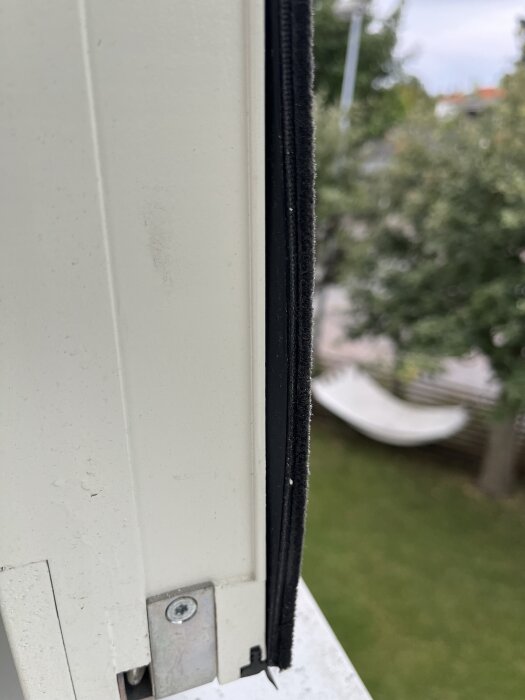 Närbild av en svart list på ett fönster från Elitfönster, monterad på en vit karm. Bakgrunden visar en trädgård med grönska.