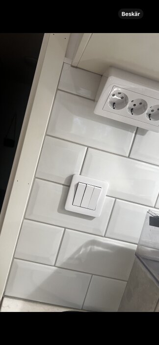 Spricka i vitt kökskakel nära dörrlist och eluttag, diskussion om rätt sätt att foga och eventuell reklamation mot plattsättaren.