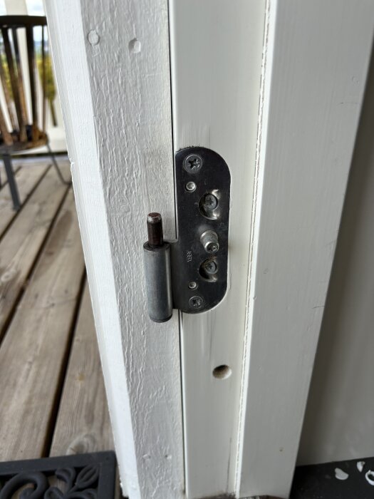 Ytterdörrens karm med bleck och justerskruvar, vitmålade ytor och trätrall i bakgrunden.