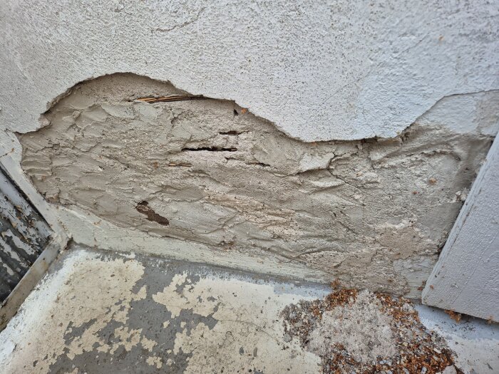 Bilden visar en balkongvägg med sprucken och flagnande puts, där en tidigare lagning är synlig.