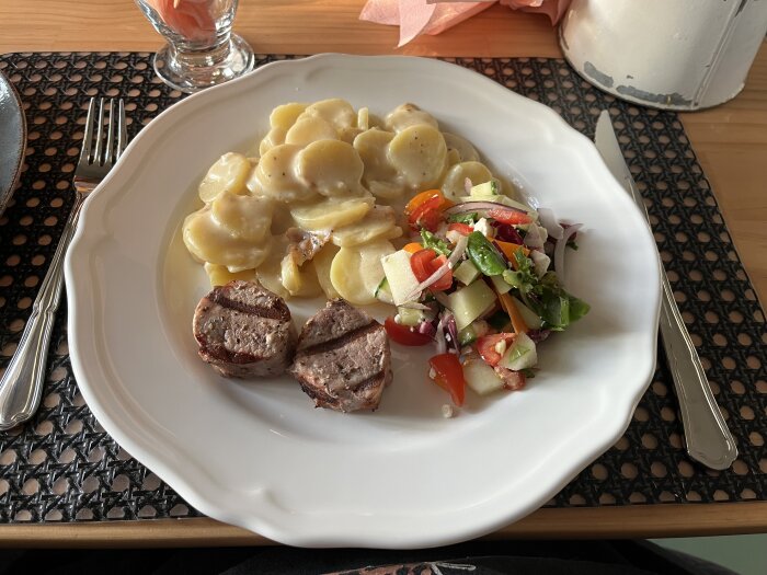 Grillad fläskfilé med potatisgratäng och färgglad sallad serverad på en vit tallrik, bestick på sidan.