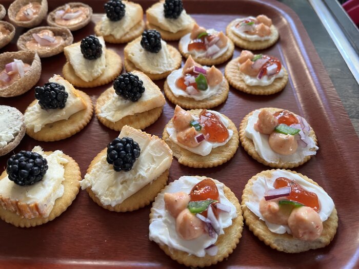 Kex med brie och björnbär samt kex med krämig röra toppad med lök, paprika och kanske hjortronsylt på en bricka.