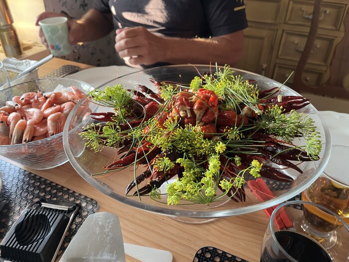 Skål med kräftor dekorerade med dillkvistar bredvid en skål med räkor på ett dukat bord.