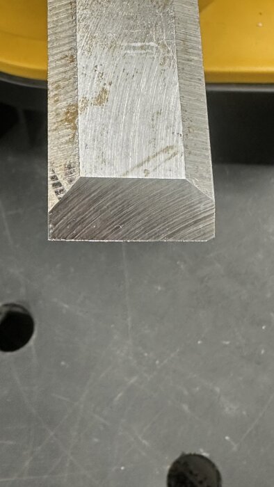 Närbild av en slipad yta på ett metallverktyg, med jämna slipmärken och fasad kant, monterat på en arbetsbänk.