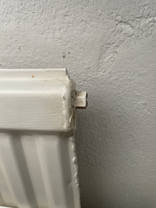 En del av en vit radiator utan termostat, fäst vid en vägg.
