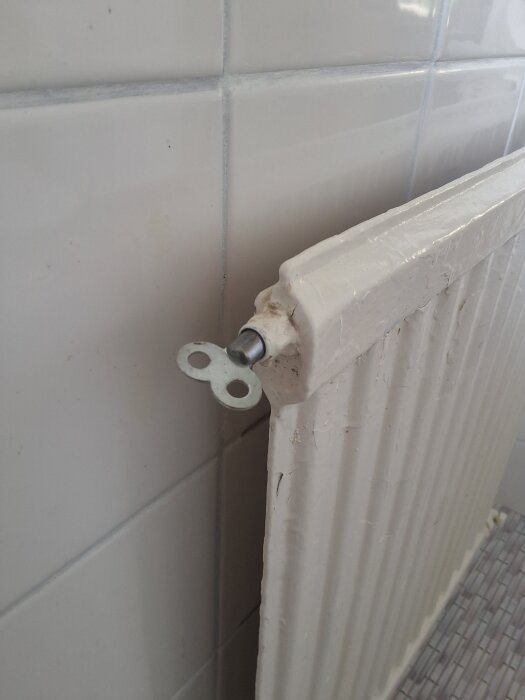 Värmeelement mot vit kakelvägg med ventil för avluftning.