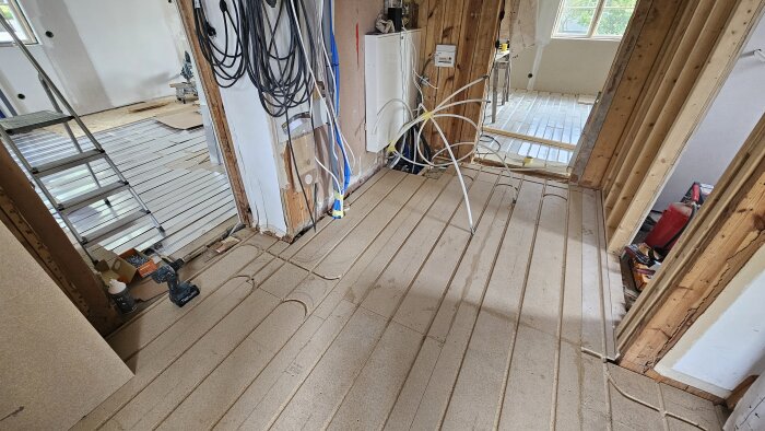 Golvet visar installerad golvvärmeinfästning på bottenplan i ett hus, med synliga rör och verktyg i närheten under renovering.