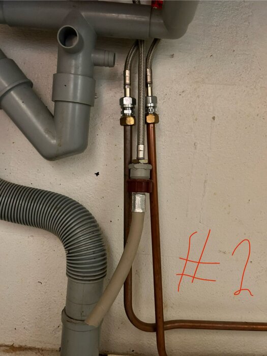 Vattenanslutning under diskbänk med plaströr, kopparrör och kopplingar, märkta med röd text "#2".