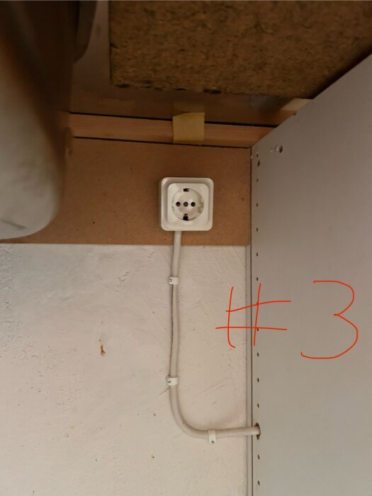 Vägguttag under köksbänk med vit elkabel som löper från uttaget.