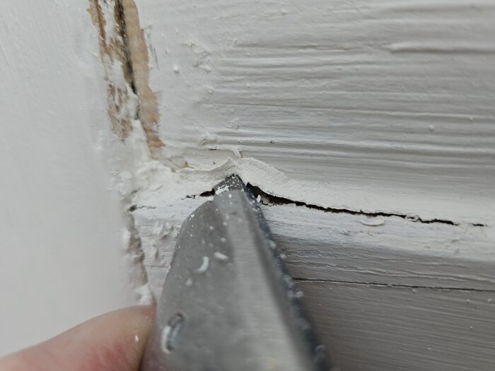 Verktyg skrapar färg från dörr med synlig flexibel fog under.