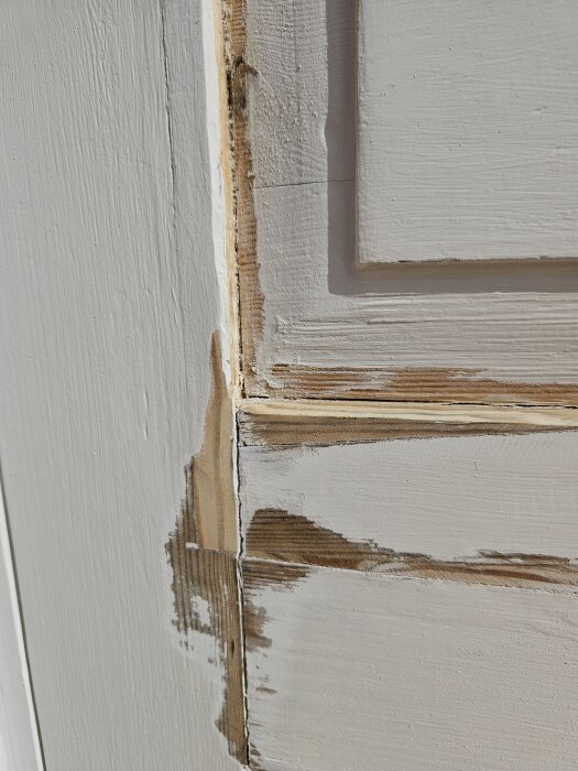 Delvis skrapad ytterdörr med gammal alkydfärg och synlig fog i hörnet, förberedd för ommålning.