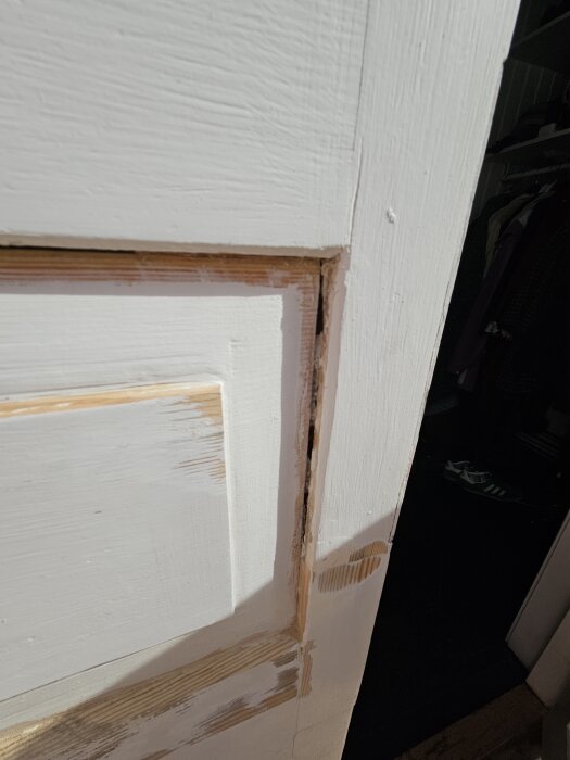 Närbild på en vit ytterdörr under reparation, avslöjar fogmaterial mellan träpaneler som delvis har skrapats före målning.