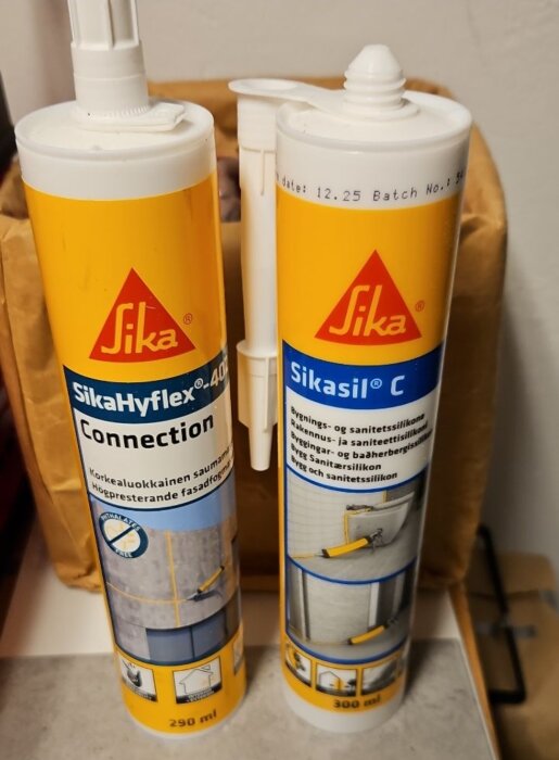 Två tuber med byggsilikon; SikaHyflex 402 Connection och Sikasill C, stående bredvid varandra på ett bord.