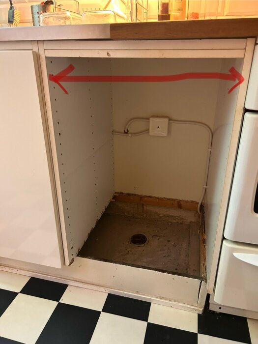 Tomt köksskåp med röda pilar som visar mätning mellan stommar, golvbrunn synlig, vägguttag och rör installation.