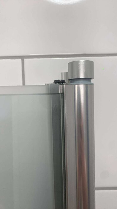 Glasvägg till dusch som har glidit ner från metallram, synlig montering i övre del mot kaklad vägg.