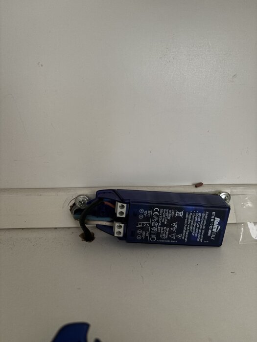 En blå transformator monterad på en vit yta, med inkopplade svarta och vita kablar.