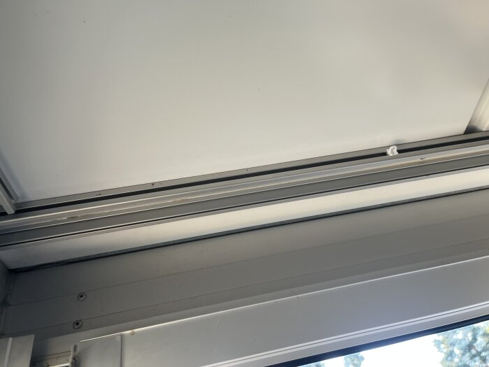 Gardinskena i taket på en inglasad balkong, med fokus på skenans monteringsdetaljer och en vit krok.