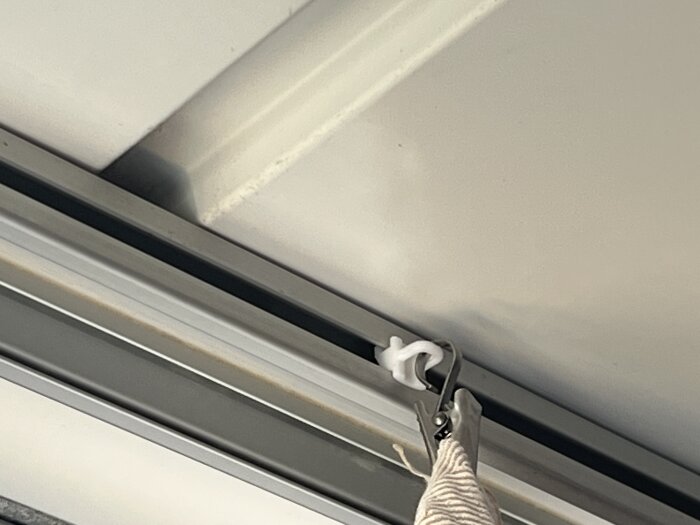 Gardinfäste i skena i balkongtak, närbild av gardinkrok och tyg hänger från skenan.