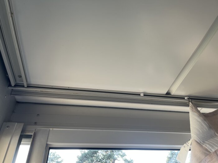 Inglasad balkong med takmonterad gardinskena och gardin fäst i skenan; användaren har problem med att dra gardinen smidigt.