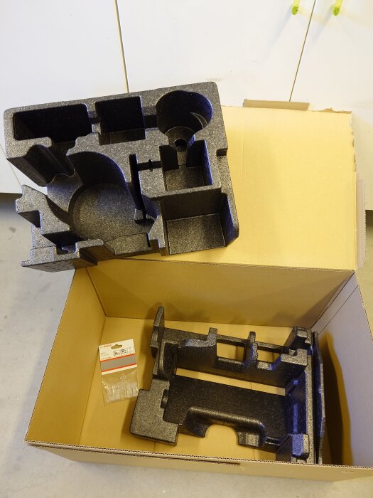 Svart L-boxx insats och förpackning med splitterskydd ligger i en kartong.