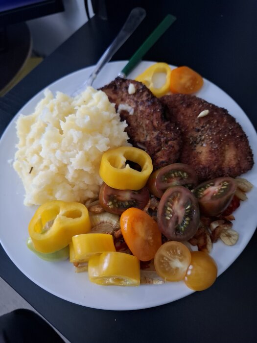 Fläskschnitzel med potatismos, gul paprika och skivade tomater på en vit tallrik.