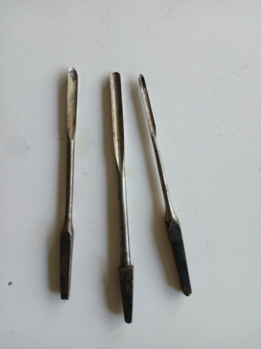Tre metallverktyg med spetsiga ändar ligger på en ljus yta.