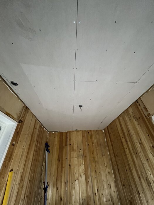 Gipstak i barnrum med träpanel på väggarna. Takdosor justerade med träpinnar för att passa nivå med gipsskivorna.