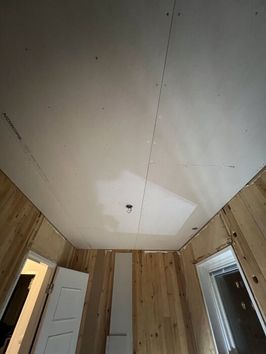 Gipsat tak i barnrum med träpanel på väggarna. Takdosor monterade med hjälp av träpinnar. Dörr och fönster syns i rummet.