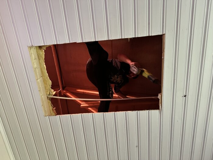 Person installerar en vindslucka och använder en såg. Taken är öppnat med isolering synlig runt kanten av öppningen.