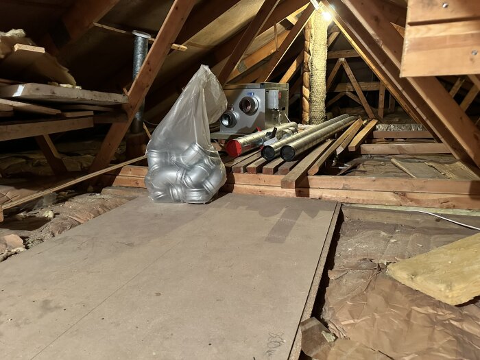 Vind med träbjälklag, FTX-systemet och ventilationsrör, samt en plastpåse full med förpackningar.