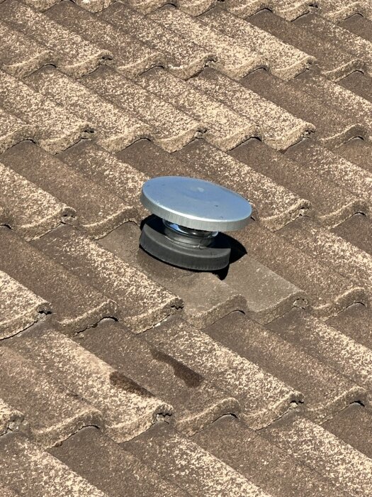 Tak med takpannor och en ventilationshuv som bryter genom en pannrad, inspekterat vid renoveringsarbete i huset.