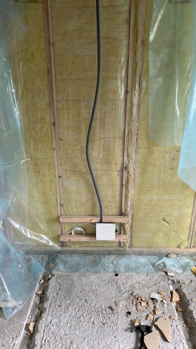 Isolerad vägg med plastskivor och kablar under renovering, stökigt golv med bråte och verktyg.