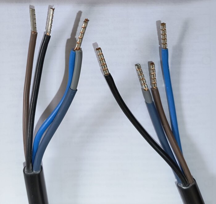 Kablar med exponerade ändar och diverse trådfärger, inklusive brun, blå och svart, ligger på ett vitt underlag.