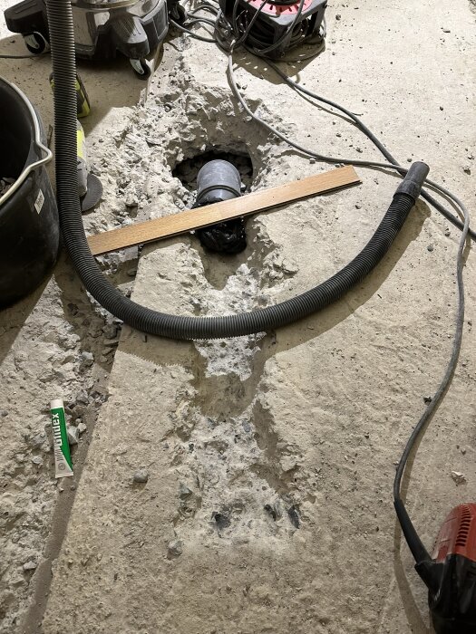 Bebetonggolv med uppbilning för avloppsrör, dammsugarslang och elektriska kablar synliga i bilden under en renovering.