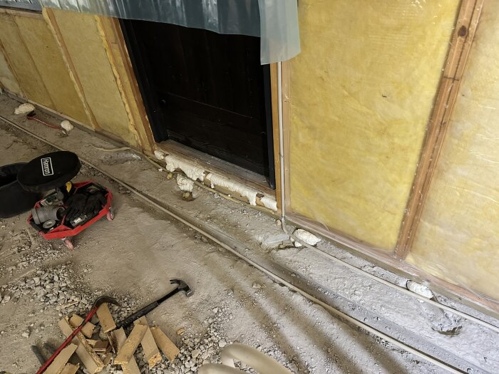 Renoveringsprojekt med bilat golv, isolerade väggar och verktyg på en röd bricka, samt träbitar och en hammare på golvet.