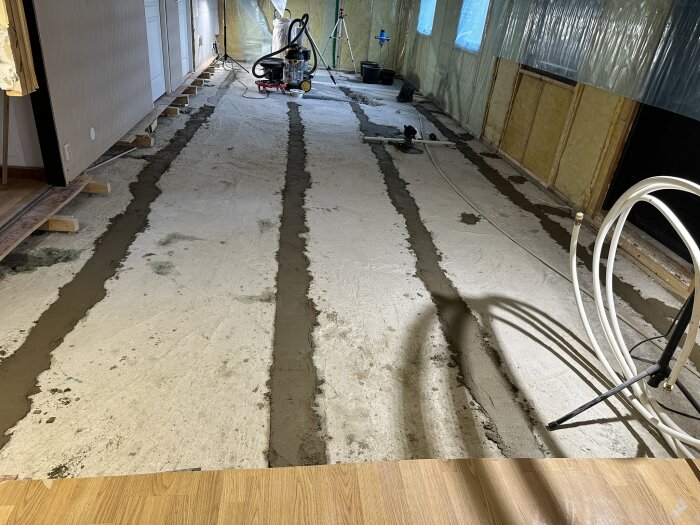Översiktsbild av renoveringssituation med ny bilning för avloppsrör. Golvet är delvis återfyllt och plastad vägg syns i bakgrunden. 5 november 2024.