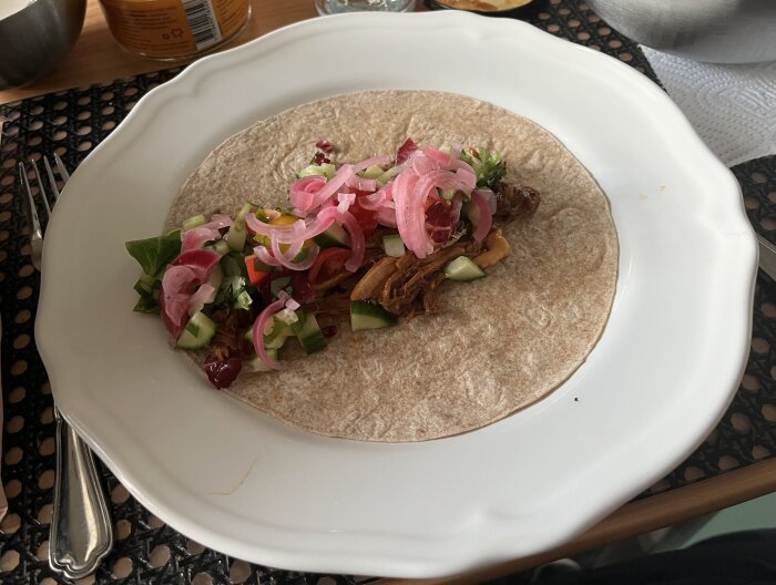 Tallrik med tortilla fylld med pulled pork, picklad rödlök, grönsaker och sallad. Serverad i en hemtrevlig miljö.