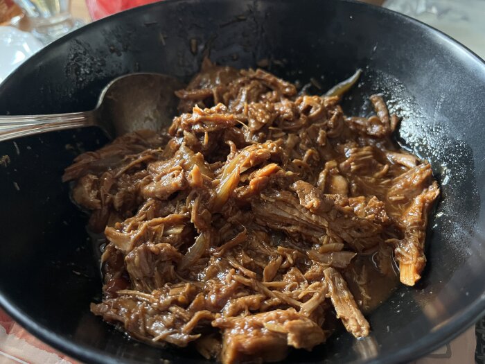 Pulled pork i en svart skål med en sked, del av en middag med ostsås, chili och grönsaker, från gårdagens måltid.