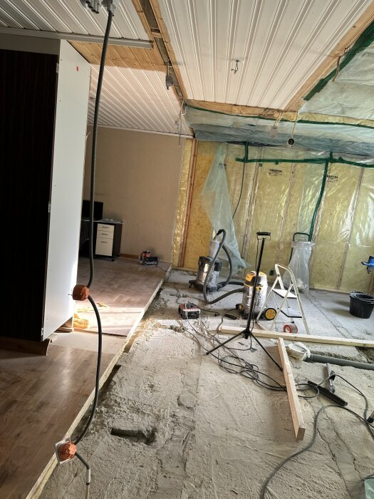 Översiktsbild av renovering med delvis riven golv, verktyg och plastad vägg, tagen den 5 november 2024; eldragningar syns i taket.