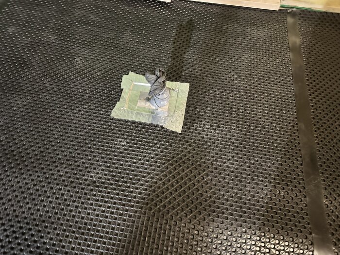 Installation av Jape Ventgolvmatta med rörgenomföring täckt av tejp och kantband, synlig på ett perforerat golvunderlag.