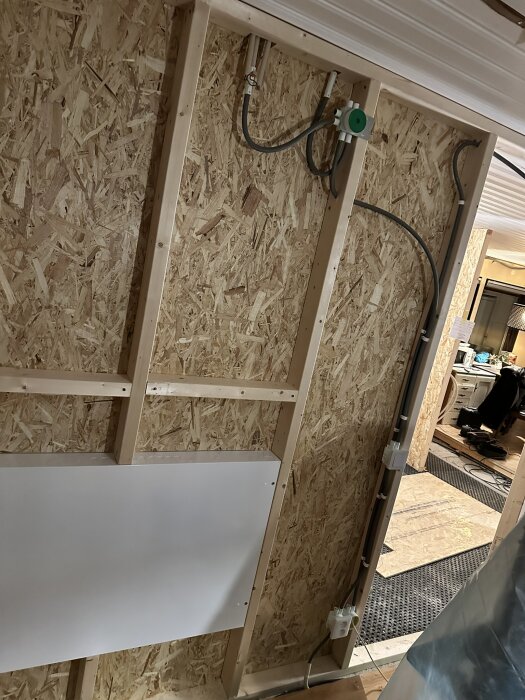 Vägg med reglar och OSB-skiva samt dragna rör, i en byggarbetsmiljö med synliga verktyg och material för installation.