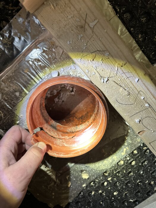 Brutet orange PVC-rör i ett byggprojekt där en övergångsdel har spruckit, omgiven av trä och byggmaterial.