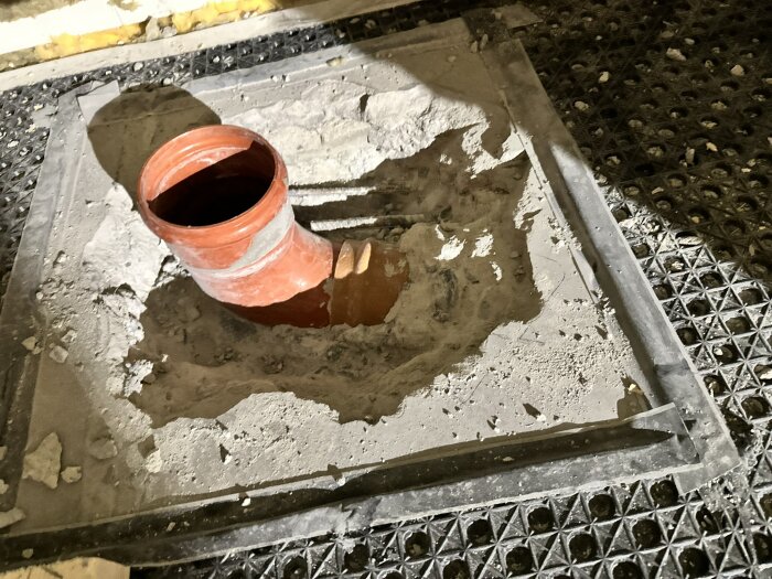 Orange PVC-avloppsrör delvis inbäddat i cement med sprickor runtom; del av ett badrumsrenoveringsprojekt.