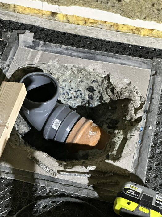 Skadat PVC-rör i betonggolv med synliga sprickor och verktyg nära, visar arbete för att reparera röranslutning till toalettsystemet.